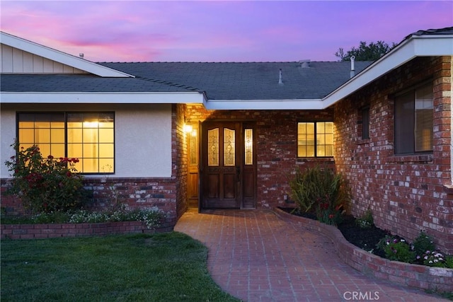320 Casa Real Pl, Nipomo, CA 93444 - exterior entry at dusk with brick siding, stucco siding, a lawn, and roof with shingles