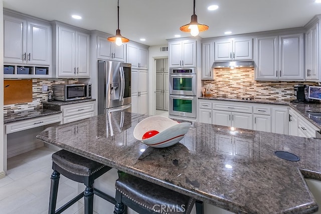 19520 Bermudas St, Porter Ranch, CA 91326 - kitchen featuring stainless steel appliances, decorative backsplash, under cabinet range hood, a breakfast bar area, and hanging light fixtures