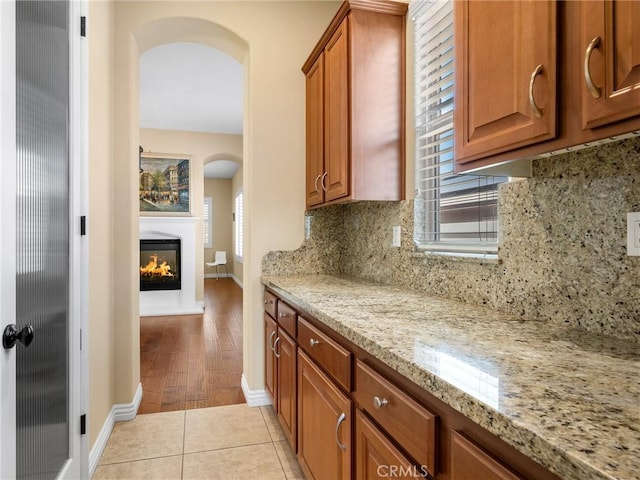 7219 Evening Star Rose Ct, Oak Hills, CA 92344 - kitchen with arched walkways, a glass covered fireplace, brown cabinetry, and decorative backsplash