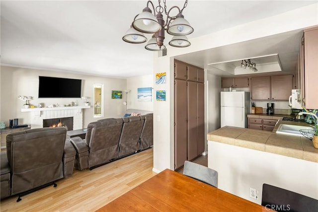 400 Brighton Spgs, Costa Mesa, CA 92627 - kitchen featuring white appliances, a chandelier, light wood-style floors, open floor plan, and a warm lit fireplace