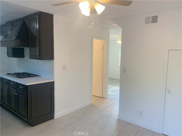 14299 La Paz Dr Unit 6, Victorville, CA 92395 - kitchen featuring custom exhaust hood, stainless steel gas cooktop, a ceiling fan, dark cabinets, and light countertops