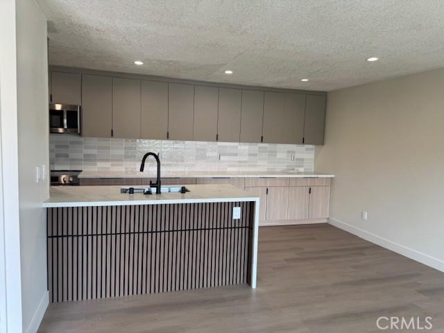 2501 W Sunflower Unit F12, Santa Ana, CA 92704 - kitchen featuring stainless steel microwave, gray cabinets, tasteful backsplash, wood finished floors, and recessed lighting