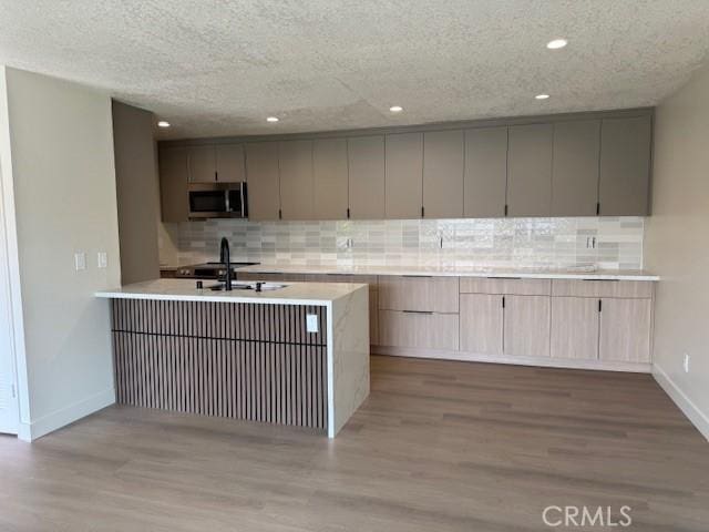2501 W Sunflower Unit F12, Santa Ana, CA 92704 - kitchen with stainless steel microwave, tasteful backsplash, wood finished floors, light countertops, and recessed lighting
