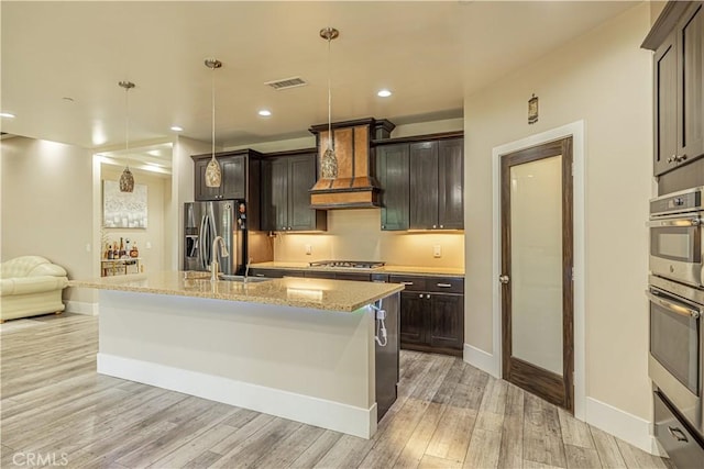 4664 Quartz Hill Rd, Quartz Hill, CA 93536 - kitchen with stainless steel appliances, custom range hood, light wood-type flooring, a center island with sink, and light stone countertops