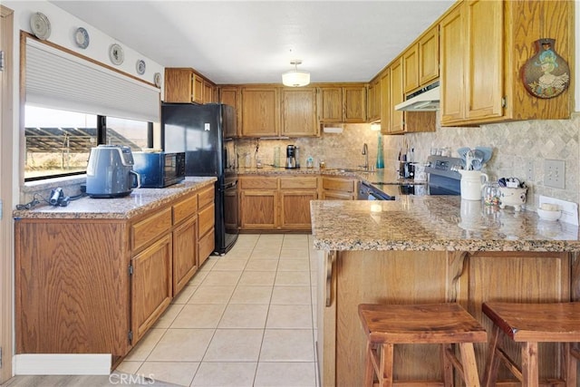 15761 Joshua Rd, Apple Valley, CA 92307 - kitchen with under cabinet range hood, black appliances, light tile patterned floors, a peninsula, and tasteful backsplash