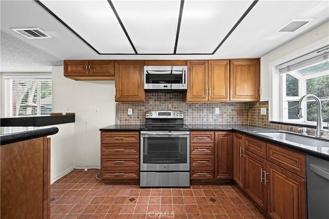 6741 Caro St, Paramount, CA 90723 - kitchen featuring stainless steel appliances, dark countertops, backsplash, brown cabinetry, and plenty of natural light