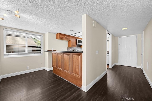 6741 Caro St, Paramount, CA 90723 - kitchen with stainless steel microwave, dark wood finished floors, a textured ceiling, brown cabinets, and dark countertops