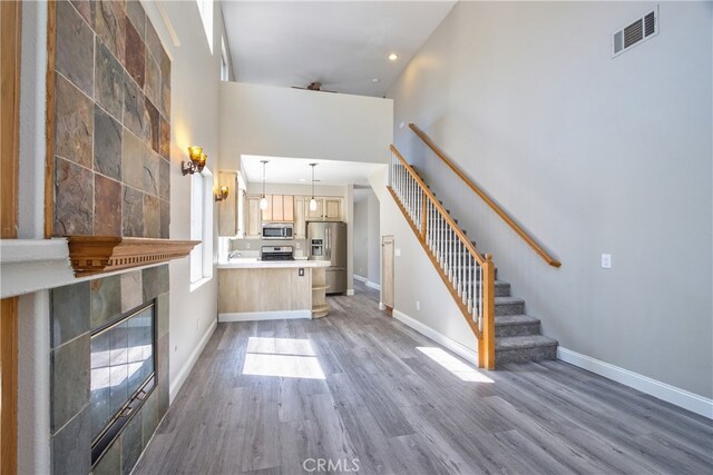 41808 Vardon Dr, Temecula, CA 92591 - unfurnished living room featuring stairway, wood finished floors, a towering ceiling, a tiled fireplace, and recessed lighting