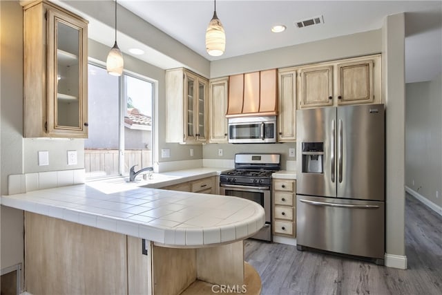 41808 Vardon Dr, Temecula, CA 92591 - kitchen with appliances with stainless steel finishes, glass insert cabinets, light brown cabinets, a peninsula, and light wood-type flooring