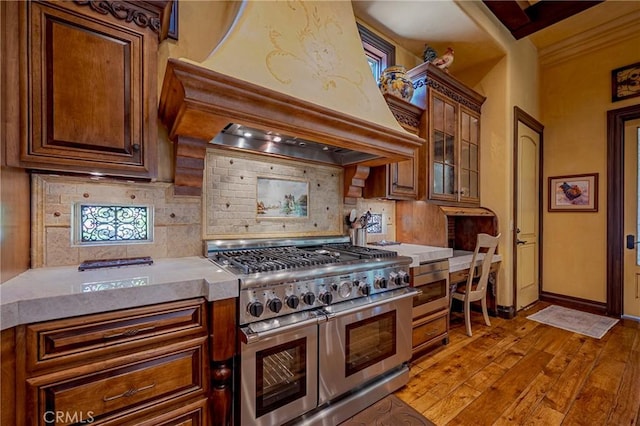 2882 Trovare Ct, Merced, CA 95340 - kitchen with range with two ovens, custom range hood, decorative backsplash, light countertops, and light wood finished floors