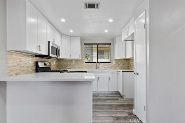 2621 E 20th St Unit 12, Signal Hill, CA 90755 - kitchen with stainless steel appliances, wood finished floors, white cabinets, recessed lighting, and a peninsula