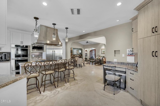 9999 Wornom Ave, Sunland, CA 91040 - kitchen with built in appliances, arched walkways, a kitchen breakfast bar, light stone counters, and recessed lighting