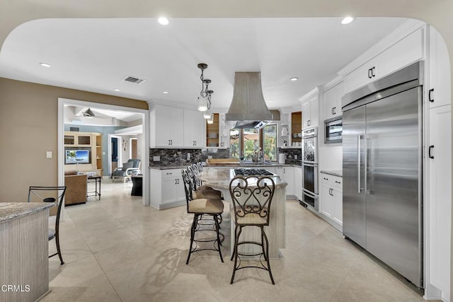9999 Wornom Ave, Sunland, CA 91040 - kitchen featuring built in appliances, a kitchen breakfast bar, tasteful backsplash, island range hood, and white cabinetry