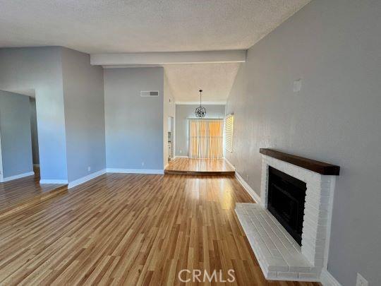 2748 Delmar Ave, Mojave, CA 93501 - unfurnished living room featuring a brick fireplace, wood finished floors, a textured ceiling, and a chandelier