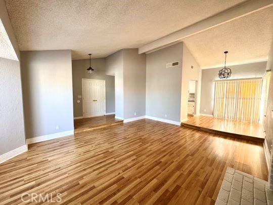 2748 Delmar Ave, Mojave, CA 93501 - unfurnished living room featuring vaulted ceiling, wood finished floors, a textured ceiling, and a chandelier