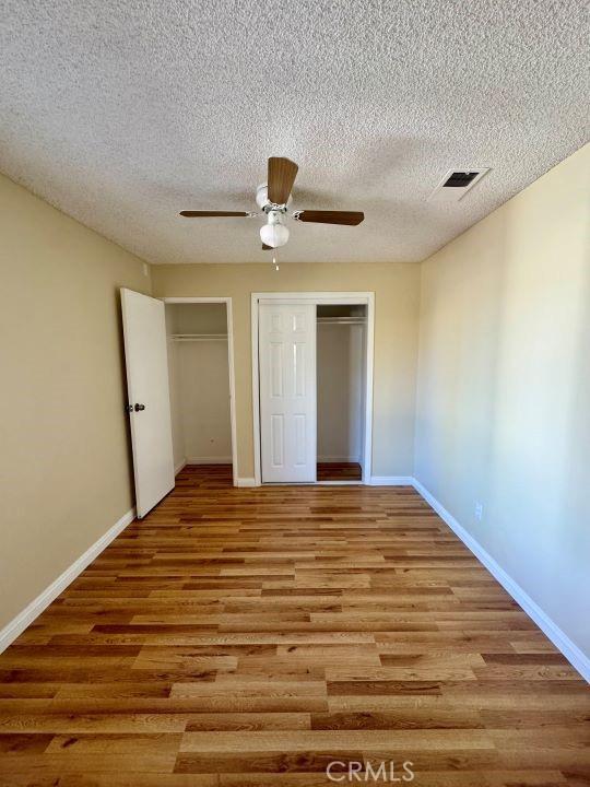 2748 Delmar Ave, Mojave, CA 93501 - unfurnished bedroom featuring wood finished floors, two closets, a textured ceiling, and a ceiling fan