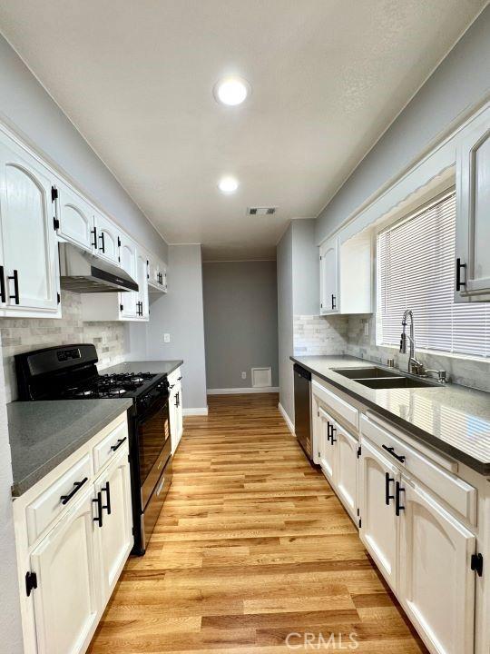 2748 Delmar Ave, Mojave, CA 93501 - kitchen with under cabinet range hood, black gas range, dishwasher, tasteful backsplash, and white cabinetry