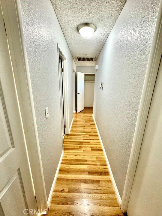 2748 Delmar Ave, Mojave, CA 93501 - corridor featuring a textured wall, light wood finished floors, and a textured ceiling