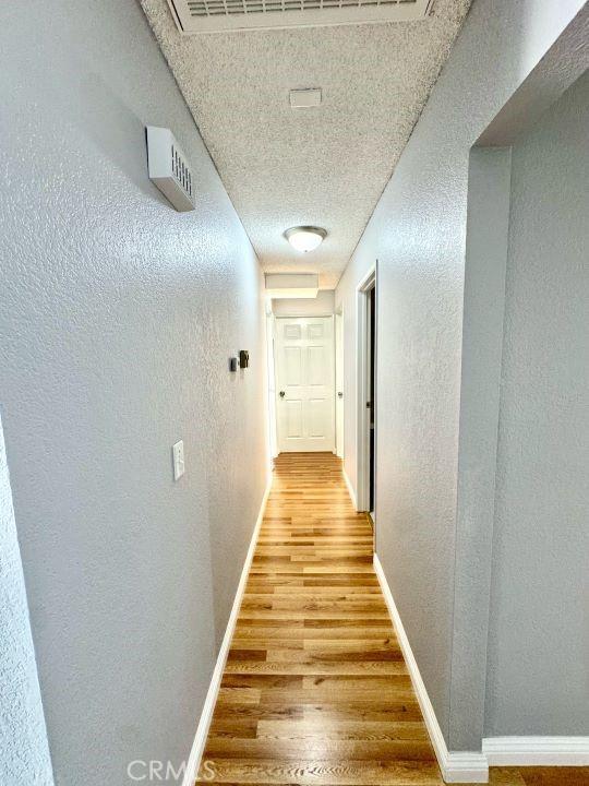 2748 Delmar Ave, Mojave, CA 93501 - corridor with light wood-type flooring, a textured wall, and a textured ceiling