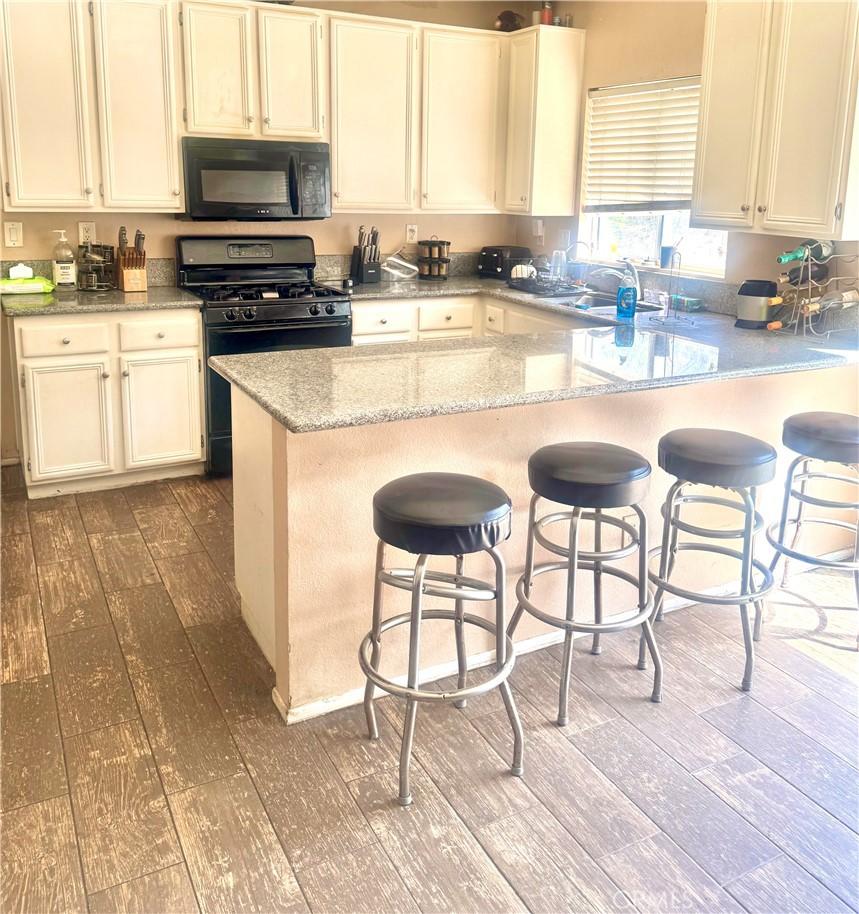 44686 Calle Hilario, Temecula, CA 92592 - kitchen with black appliances, wood-type flooring, light stone counters, a breakfast bar area, and a peninsula