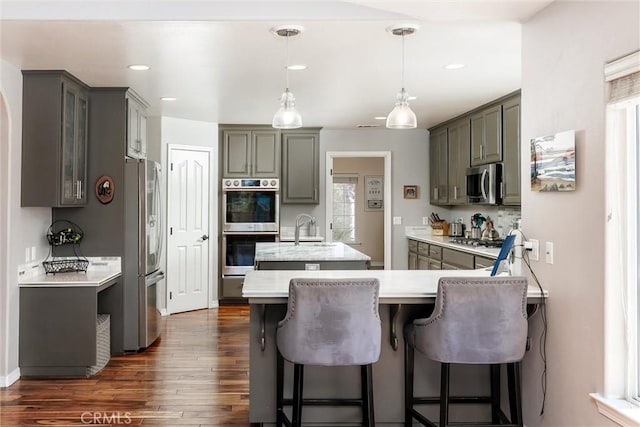 620 Camino Roble, Nipomo, CA 93444 - kitchen with appliances with stainless steel finishes, a peninsula, dark wood-style floors, a kitchen island with sink, and decorative light fixtures