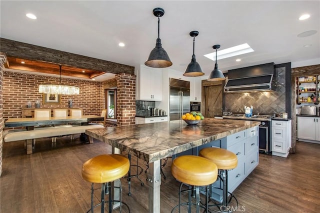 27151 Mission Hills Dr, San Juan Capistrano, CA 92675 - kitchen with stainless steel appliances, wall chimney exhaust hood, dark countertops, dark wood-type flooring, and brick wall