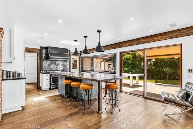 27151 Mission Hills Dr, San Juan Capistrano, CA 92675 - kitchen featuring wall chimney exhaust hood, dark countertops, light wood-type flooring, a breakfast bar, and recessed lighting