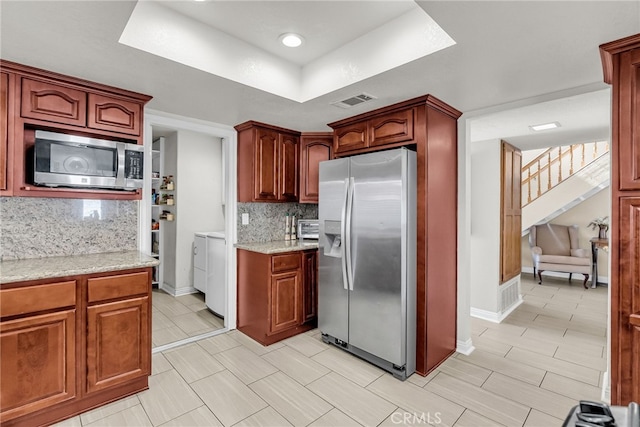13180 Meteor Dr, Victorville, CA 92395 - kitchen with stainless steel appliances, independent washer and dryer, a tray ceiling, decorative backsplash, and light stone countertops