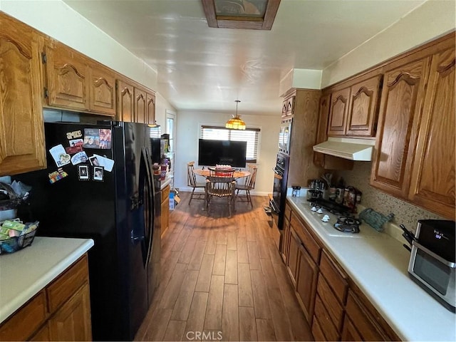 13431 Olympus Dr, Westminster, CA 92683 - kitchen featuring black appliances, under cabinet range hood, dark wood finished floors, light countertops, and brown cabinets