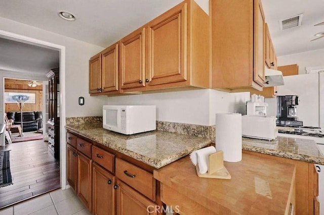 665 N Waterbury Ave, Covina, CA 91722 - kitchen with white microwave, light stone counters, brown cabinets, exhaust hood, and light tile patterned flooring
