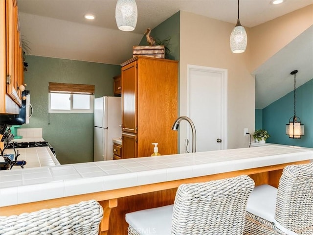 271 Vista Del Mar Unit 1, San Simeon, CA 93452 - kitchen with freestanding refrigerator, tile counters, a breakfast bar, brown cabinetry, and decorative light fixtures
