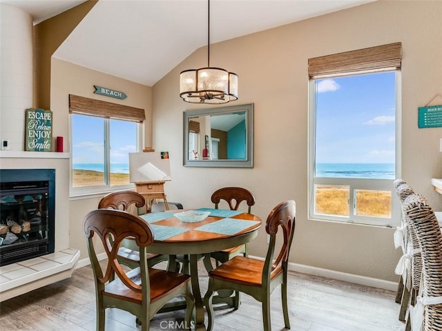 271 Vista Del Mar Unit 1, San Simeon, CA 93452 - dining room featuring wood finished floors, a chandelier, a glass covered fireplace, vaulted ceiling, and a water view