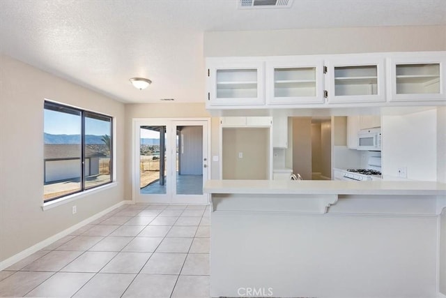 7267 Dalscote St, Hesperia, CA 92345 - kitchen with white microwave, light countertops, white cabinetry, glass insert cabinets, and light tile patterned floors