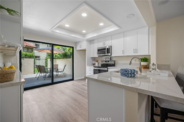 18325 Gum Tree Ln, Huntington Beach, CA 92646 - kitchen featuring stainless steel appliances, a raised ceiling, a peninsula, light stone countertops, and light wood-type flooring