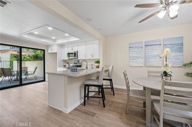 18325 Gum Tree Ln, Huntington Beach, CA 92646 - kitchen with appliances with stainless steel finishes, light wood-style flooring, a peninsula, a tray ceiling, and recessed lighting