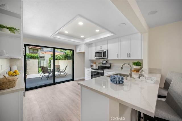 18325 Gum Tree Ln, Huntington Beach, CA 92646 - kitchen with appliances with stainless steel finishes, a peninsula, a tray ceiling, light wood-style floors, and open shelves