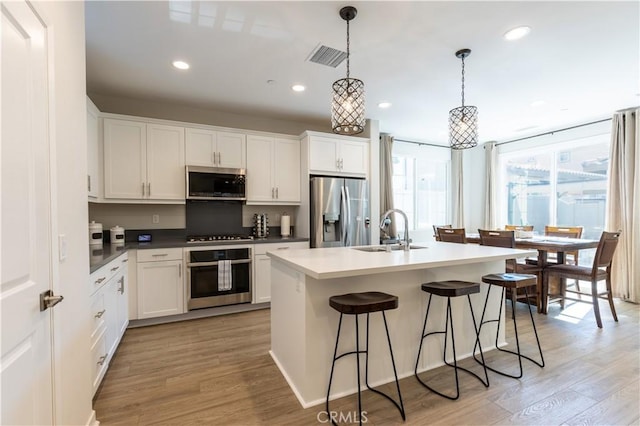 45055 Via Vela, Temecula, CA 92592 - kitchen with appliances with stainless steel finishes, light wood-style floors, a breakfast bar area, white cabinetry, and a center island with sink