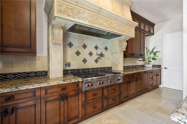 1377 Versante Cir, Corona, CA 92881 - kitchen featuring premium range hood, stainless steel gas cooktop, tasteful backsplash, light stone countertops, and glass insert cabinets