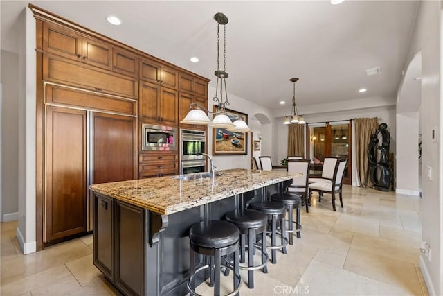1377 Versante Cir, Corona, CA 92881 - kitchen with built in appliances, arched walkways, recessed lighting, light stone counters, and a center island with sink
