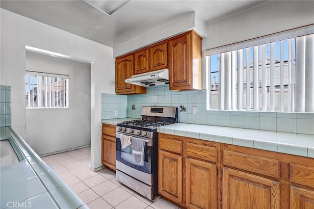 17959 Cantara St, Reseda, CA 91335 - kitchen featuring stainless steel gas range oven, under cabinet range hood, brown cabinetry, light tile patterned floors, and tasteful backsplash