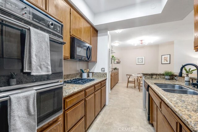 3284 Barham Blvd Unit 201, Los Angeles, CA 90068 - kitchen with black appliances, brown cabinetry, a tray ceiling, light stone countertops, and light tile patterned flooring