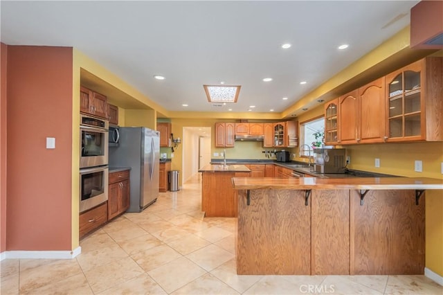 2935 Athel Dr, Hacienda Heights, CA 91745 - kitchen featuring appliances with stainless steel finishes, a peninsula, a kitchen breakfast bar, under cabinet range hood, and glass insert cabinets