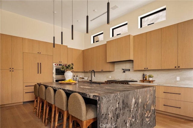 1955 Curson Pl, Los Angeles, CA 90046 - kitchen featuring light brown cabinets, double oven, a towering ceiling, dark stone counters, and a kitchen bar