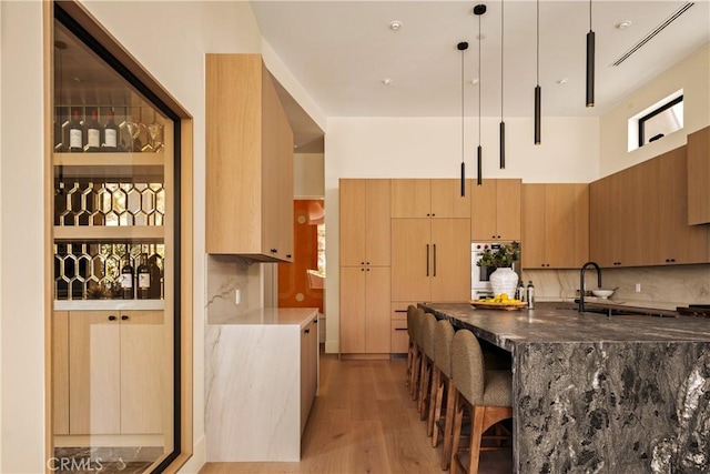 1955 Curson Pl, Los Angeles, CA 90046 - kitchen featuring dark stone counters, light wood-type flooring, tasteful backsplash, a breakfast bar area, and modern cabinets