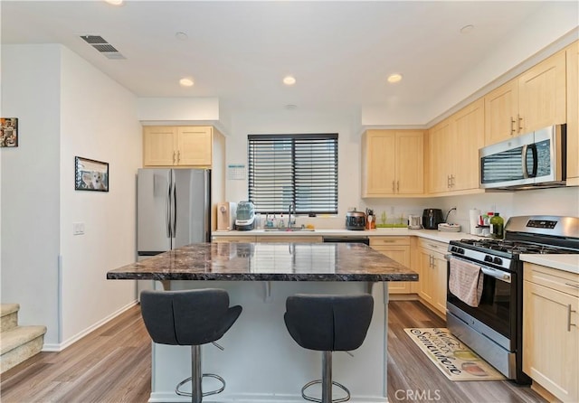 677 Savi Dr Unit 101, Corona, CA 92878 - kitchen featuring appliances with stainless steel finishes, light brown cabinets, a kitchen bar, wood finished floors, and recessed lighting