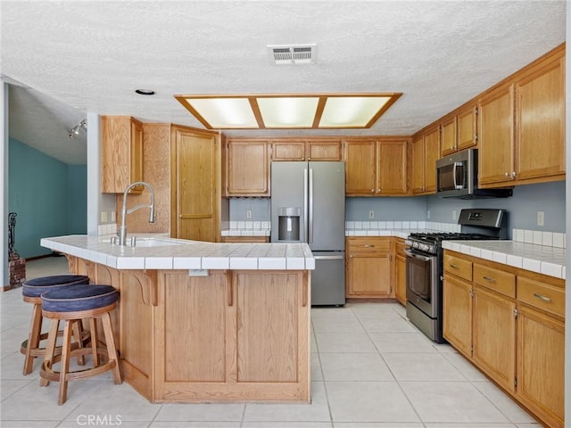 7556 Glider Ave, Hesperia, CA 92345 - kitchen featuring stainless steel appliances, a peninsula, a kitchen breakfast bar, a textured ceiling, and light tile patterned flooring