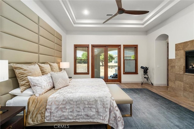 54774 Bautista Rd, Anza, CA 92539 - bedroom with a tray ceiling, arched walkways, a tile fireplace, wood finished floors, and a ceiling fan