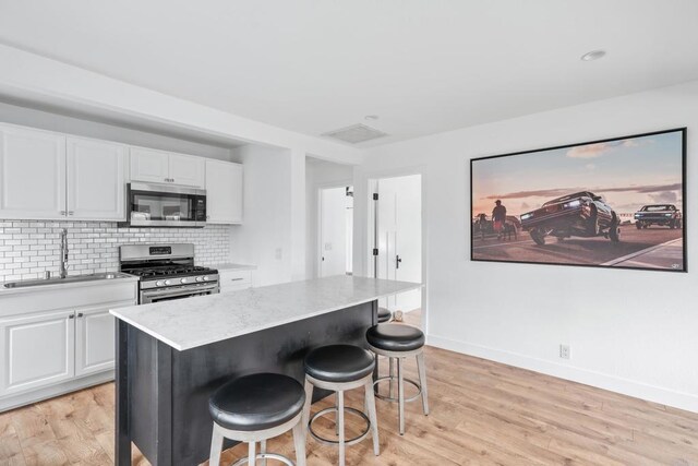 1009 S Cleveland St, Oceanside, CA 92054 - kitchen featuring appliances with stainless steel finishes, white cabinetry, a breakfast bar area, and light wood-type flooring