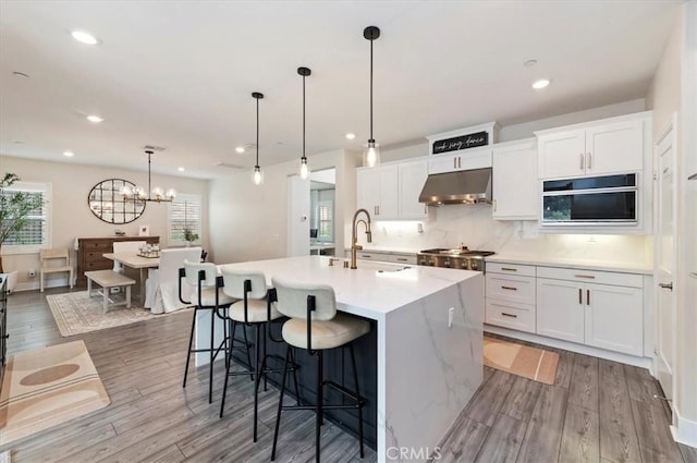 2516 Chad Zeller Ln, Corona, CA 92882 - kitchen featuring under cabinet range hood, wood finished floors, light countertops, a kitchen island with sink, and white cabinetry