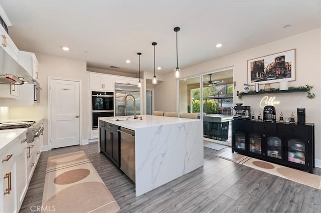 2516 Chad Zeller Ln, Corona, CA 92882 - kitchen featuring appliances with stainless steel finishes, wood finished floors, white cabinets, an island with sink, and wall chimney range hood